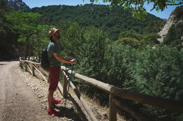 Etrafı yemyeşil dağlarla çevrili, maceralı ve aktif bir yaşam tarzı olan bir yolda yürüyen bir adam. Sırt çantası ve bastonları açık hava keşfi ve doğa tutkusunu gösteriyor..
