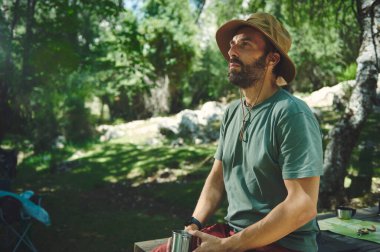 Ağaçların arasından süzülen güneş ışığıyla gölgeli bir ormanda doğanın huzurunun tadını çıkaran bir adamın huzurlu anı. Açık hava eğlencesi ve rahatlığının mükemmel bir temsilidir..