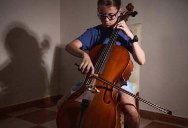 Genç bir insan içeride çello çalıyor ve dikkatle performansına odaklanıyor. Dekor, bu güzel enstrümanda ustalaşmaya olan bağlılıklarını ve tutkularını vurguluyor..