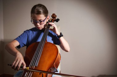 Genç bir müzisyen içeride sakin bir ortamda çello çalıyor, alıştırma sırasında odak ve adanmışlık gösteriyor. Odanın rahatlatıcı atmosferi sanatsal ifade tutkusunu vurguluyor.