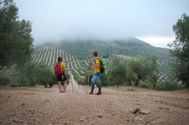 Renkli sırt çantaları ve yürüyüş direkleriyle iki yürüyüşçü puslu bir gökyüzü altında manzaralı manzaraları keşfederek doğada macerayı kucaklıyor. Bu görüntü dışarıdaki keşiflerde dolaşma şehveti ve sükuneti çağrıştırıyor..