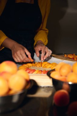Bir kadın pasta tabağında taze dilimlenmiş kayısılar hazırlıyor. Kayısı kâseleriyle vurgulanıyor. Sıcak ve yaratıcı bir mutfak ortamı yaratıyor..