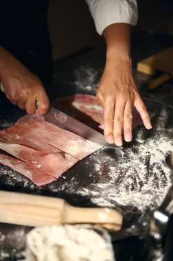 Bir şef pembe makarna hamuru üzerinde titizlikle çalışır. Un kaplı bir çalışma alanında onu keser. Geleneksel teknikler ve İtalyan mutfak sanatını gözler önüne serer..