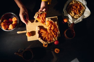Taze kayısılar ve mutfak gereçleriyle çevrili bir kayısılı tart sahnesi. Mutfak ortamında ev yapımı pişirme ve kırsal estetiğin özünü yakalar..