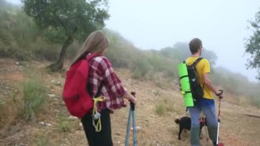 Aktif ve sağlıklı yaşam tarzı: Genç bir çift ve köpekleri sisli dağ yollarında yürüyüş yapıyorlar. Doğayı kucaklarlar. Huzurlu güzelliği. Sırt çantaları ve bastonlarıyla..
