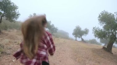 Genç Kadın, Antik Zeytin Ağaçları ile Sisli bir arazide Yapayalnız Yürüyüşün keyfini çıkarıyor, Doğanın Huzurlu Güzelliğini Kucaklıyor ve Dönen Dağ Yolunda Aktif, Sağlıklı Yaşam Tarzı.