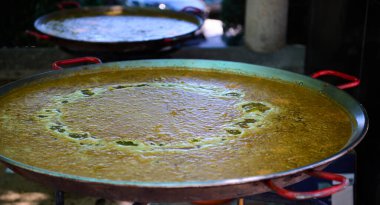 İspanyol köyündeki canlı bir festival sırasında açık havada pişirilen geniş bir paella tenceresi, paylaşılan yemek pişirme deneyimleri üzerine toplumsal kutlama, gelenek ve kültürü sergiliyor..
