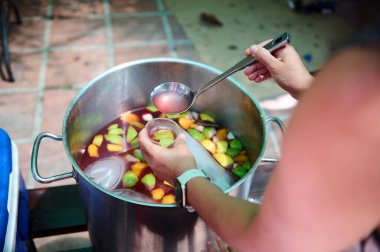 Geniş paslanmaz çelik tencere ve açık havada sunulan taze meyveler sosyalleşmenin ve ev yapımı içeceklerin keyfini çıkarmanın neşeli atmosferini betimliyor..
