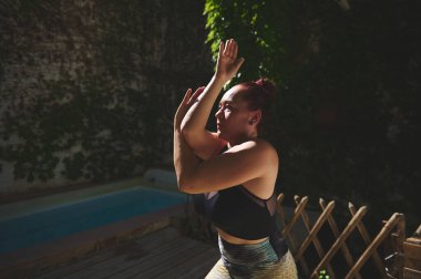 Açık havada yoga yapan bir kadın, forma ve rahatlamaya odaklanıyor, doğal ışık ortamı güçlendiriyor..