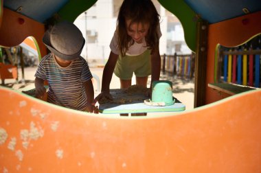 İki çocuk canlı bir oyun alanının içinde oyun oynamaktan zevk alıyor, kum havuzuyla meşgul oluyorlar. Güneşli bir gün çocukluğun ve açık hava eğlencesinin neşesini vurguluyor.