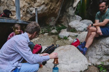 Bir grup arkadaş dışarıda toplanıyor, kayalık bir arka planda taze demlenmiş kahve yudumluyorlar. Bu yakalama, boş zamanı, dostluğu ve doğada zaman geçirmenin zevkini vurguluyor..