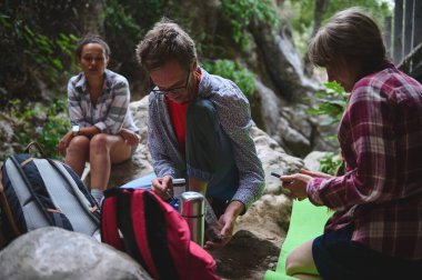 Yeşillik ve kayalarla çevrili, doğa üzerinde dinlenen bir grup arkadaş yürüyüş macerası sırasında doğa ile dostluk ve uyum sergiliyorlar..