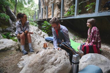 Bir grup, yürüyüş sırasında kayalar ve yeşillikler arasında vakit geçirir, kaynaşır ve yemek pişirir. Çevreleri doğa ile çevrili ve neşeli bir günde gündelik bir sohbetin tadını çıkarıyorlar..