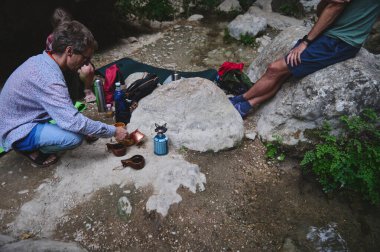 Bir grup arkadaş kahve hazırlamaktan ve kayalar ve yeşillikler arasında bir açık hava gezisinde dinlenmekten zevk alıyorlar. Sahne canlandırıcı ve doğaya yakın bir deneyimin özünü yakalıyor..