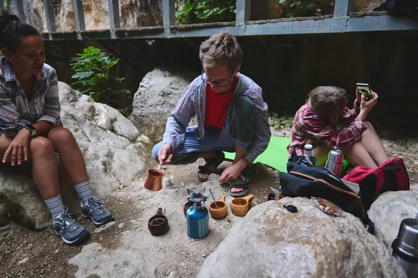 Bir grup kampçı, sık yeşilliklerin arasında oturarak açık hava kahve hazırlığının keyfini çıkarıyorlar. Görüntü, boş zamanların, arkadaşlığın ve doğadaki paylaşılan anların güzelliğinin altını çiziyor..