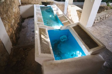 Taşlar ve betonla inşa edilmiş, berrak mavi suyla doldurulmuş ve güneş ışığıyla aydınlatılmış geleneksel bir su yalağı. Tarihi ve yerel öneme sahip kültürel ve mimari bir unsur.