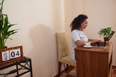 Odaklanmış bir kadın, dizüstü bilgisayarıyla iyi organize edilmiş bir ofisten çalışıyor. Çevrede bitkiler, sıcak ışıklandırma ve eğlence amaçlı konforlu ortam yer alıyor. Telekomünikasyon için ideal bir temsil