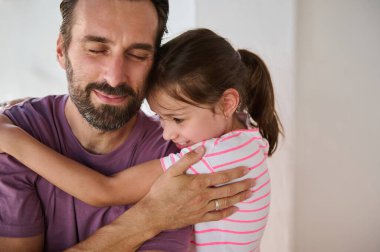 Neşeli bir baba ve kızı, sevgi ve bağın resmedildiği duygusal bir kucaklaşmayı paylaşıyor. Sahne, huzurlu bir ev ortamındaki aile bağını, hassas anları ve mutluluğu vurguluyor..