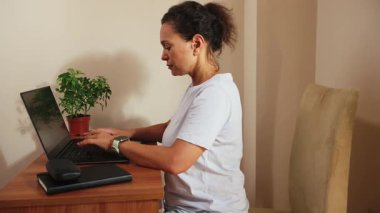 Bir kadın ev ofisinde dizüstü bilgisayarıyla yazı yazmaya odaklanmış. Uzaktan çalışma, üretkenlik ve modern dijital yaşam tarzını somutlaştırıyor. Bu video iş, çevrimiçi öğrenme ve esnek iş temaları için uygundur.