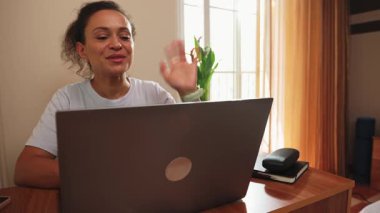 Gülümseyen kadın dizüstü bilgisayar görüntülü arama sırasında mutlu bir şekilde el sallıyor. Bu görüntüler modern uzaktan iletişimi yakalar, meslekdaşlarıyla veya müşterileriyle ilişki kuran profesyoneller için üretken ve eğlenceli bir deneyim gösterir.