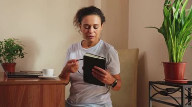 Kadın ev ofisinde uzaktan kumandayı bitiriyor. Bilgisayarı kapatıyor, rahatlatıcı bir kahve molası veriyor. Verimli bir günün ardından modern iş hayatı dengesi, konfor ve sükuneti vurgular.