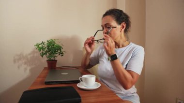 Odaklanmış bir kadın, özenle bilgisayarını kullanarak evinden uzakta çalışıyor. Gözlük takıyor, gününü planlamak için bir defter açıyor ve kahvesini yudumluyor. Bu video ev yaşamının üretken özünü yakalıyor, konforu ve modern hayatı vurguluyor.