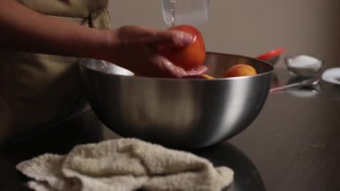 Kırsal bir mutfak ortamında paslanmaz bir kasede olgun şeftalileri yıkayan ellerin yakın plan görüntüsü. Ev yemeklerini, yemek hazırlıklarını ya da taze üretim temaları için mükemmel bir örnektir..