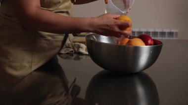 Bir insan taze bir hazırlığın altını çizerek olgun şeftalileri bir kasede temizler. Temizliği, doğal ürünleri ve mutfak aktivitelerini vurgulayan sahne, sağlıklı bir yemek hazırlama anı sunuyor..