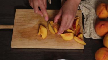 Taze, olgun şeftaliler ahşap bir kesim tahtasının üzerinde dilimleniyor. Yemek ve tatlı için mükemmel. Eller dikkatle hazırlanır, tazelik ve sağlıklı mutfak aktivitelerini anımsatır..