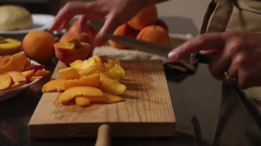 Taze portakallar ve şeftaliler ahşap bir tahtada dilimlenir ve sıcak, ev yapımı bir mutfak atmosferi yaratır. Bir el, meyveleri ustalıkla keser. Tatlı hazırlamak ya da sağlıklı atıştırmalıklar için mükemmeldir..