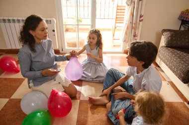 Evde toplanan bir aile, fayanslı zeminde renkli balonlarla eğlenceli aktiviteler yapmayı içerir..