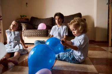 Bir grup çocuk, rahat bir oturma odasında renkli balonlarla etkileşime girip neşe ve neşe uyandırıyorlar..