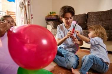 Bir aile, renkli balonları kapalı alanda birlikte şişirerek meşgul edici aktivitelerden zevk alır. Ebeveynler ve çocuklar neşeyi, kahkahayı ve yaratıcılığı paylaşıyor, neşeli bir anda bağ ve bağlantıyı teşvik ediyor..