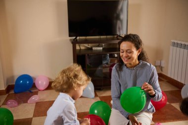 Bir anne ve çocuğu, evin içinde renkli balonlarla çevrili, neşe, bakım ve aile bağı ile dolu, yürek ısıtan bir anı paylaşıyorlar. Kutlama ve birliktelik kavramları için mükemmel..