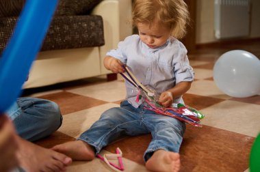 Genç bir çocuk içeride renkli oyuncaklar ve balonlarla yerde oynamaktan hoşlanır. Dekor rahat ve neşeli bir yaşam alanı gösteriyor. Neşeli ve rahat bir atmosfer yaratıyor..