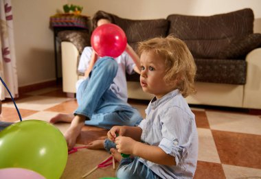 Çocuklar renkli balonlarla evin içinde neşeli anların tadını çıkarıyorlar, canlı ve neşeli bir atmosferi vurguluyorlar..