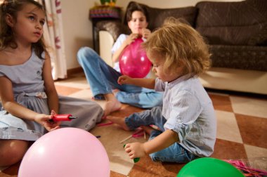 Bir grup çocuk renkli balonlar şişirmek, kahkaha ve neşe paylaşmak için sıcak bir oturma odasında toplanıyor. Kutlama, çocukluk anıları ve aile toplantıları için ideal..