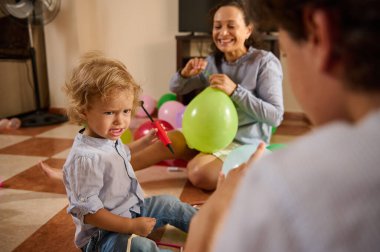 Neşeli bir aile sahnesi. Aileler ve bir çocuk balonları evde yapılacak bir kutlamaya hazırlıyorlar. Etkileşim, sevgi ve yaratıcılığı yansıtan bağlılığı, gülümsemeyi ve takım çalışmasını gösterir..