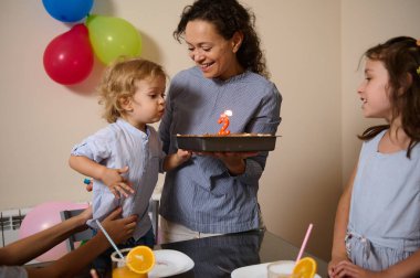 Bir çocuğun pastaya mum üfleyişini gösteren bir doğum günü partisi. Renkli balonlar, neşeli ifadeler ve o anın mutluluğunu vurgulayan parlak bir atmosfer..