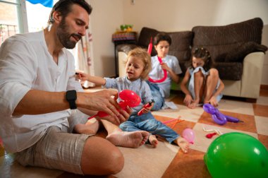 Bir baba ve üç çocuğu evde bağ kurarak balondan hayvanlar yaratıyor. Aile yerde oturuyor, renkler ve neşeyle dolu neşeli ve yaratıcı bir anın tadını çıkarıyor..