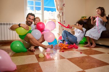 Neşeli bir aile içeride renkli balonlarla oynayarak birlikte keyifli zaman geçirir. Sahne bağ, mutluluk ve ebeveyn-çocuk etkileşiminin canlı atmosferini vurguluyor.