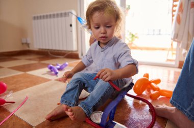 Bir bebek evde balonlarla ve oyuncak pompayla oynar. Ilık doğal ışık çekici ve eğlenceli bir atmosfer yaratır. Canlı renkler ve döşeme döşemesi canlı sahneyi vurguluyor..