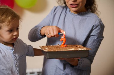 Bir çocuk ve ebeveyn, bir doğum günü kutlaması sırasında, sevgi ve ailenin birlikteliğini tasvir eden yanan bir mumla bir pasta gibi bir anı paylaşırlar..