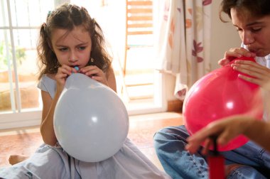 İki çocuk kapalı bir odada eğlenceli bir aktivitenin keyfini çıkarıyor. Sıcak bir odada renkli balonlar şişiriyorlar..