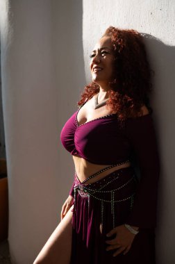 Şık bir kadın, beyaz bir duvara karşı güven içinde poz veriyor, zarafet ve tarz sergiliyor. Canlı kişiliği ve şık giyiminin altını çizen doğal ışıklandırmayla mükemmel bir şekilde yakalanmış..