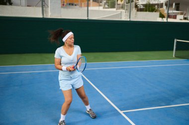 Sporcu bir kadın açık havada tenis raketi sallayarak enerji ve beceri sergiliyor..