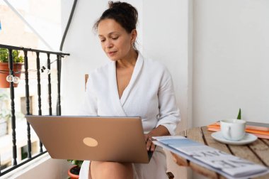 Rahat bir ortamda, doğal elementlerle çevrili bir balkonda dizüstü bilgisayar kullanan bir kadın sakin ve üretken bir atmosfer yaratıyor..