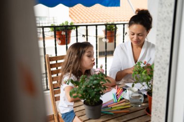 Bir anne ve kız, bitkilerle çevrili güneşli bir balkonda yaratıcı bir çizim seansının keyfini çıkarırlar. Sahne, sanat ve birliktelikle dolu neşeli ve samimi bir aile anını yansıtıyor..