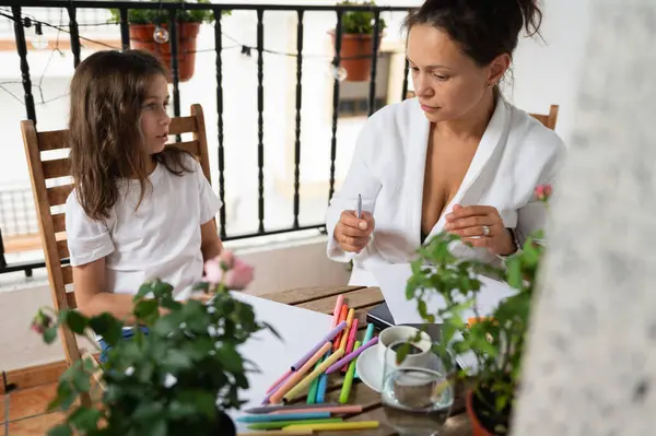 Bir anne ve kızı, bağlarını güçlendirmek için bir avluda sanat ve zanaat icra ediyorlar. Açık hava ortamında bitkiler ve renkli malzemeler var, sıcak ve neşeli atmosfere ekleniyor..