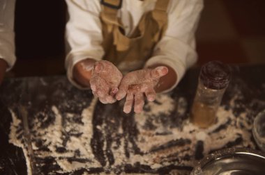 Un, elleri hamuru sunarken yüzeyin tozunu alır, kavanozlar ve pişirme aletleriyle çevrili, sıcak bir ev pişirme anını yakalar ve sıcak bir mutfak hissi verir..
